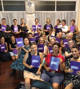 A group of women and non-binary people holding up copies of a report